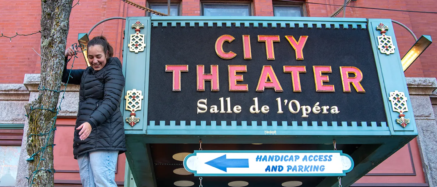 A student on a ladder putting holiday lights around a tree in front of a sign that reads, "City Theater"