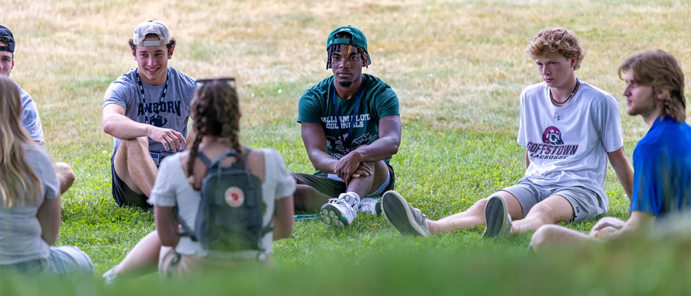 Several students talk while sitting in green grass