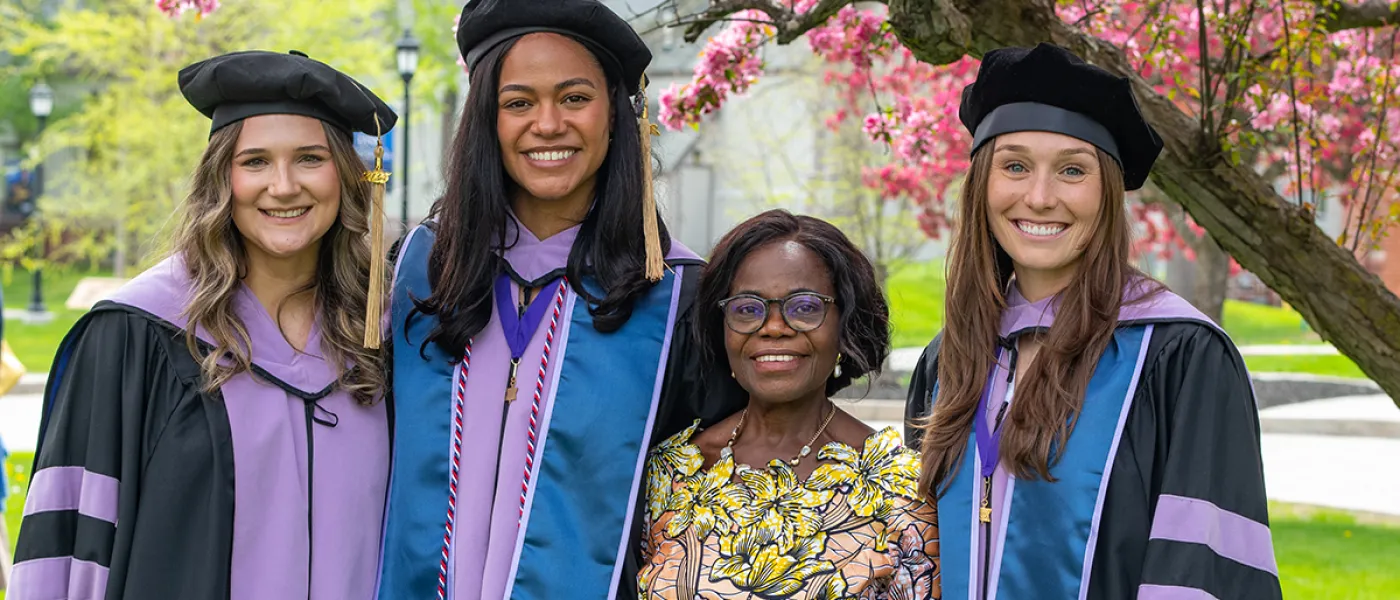 A group of C D M graduates pose in front of a cherry blossom tree