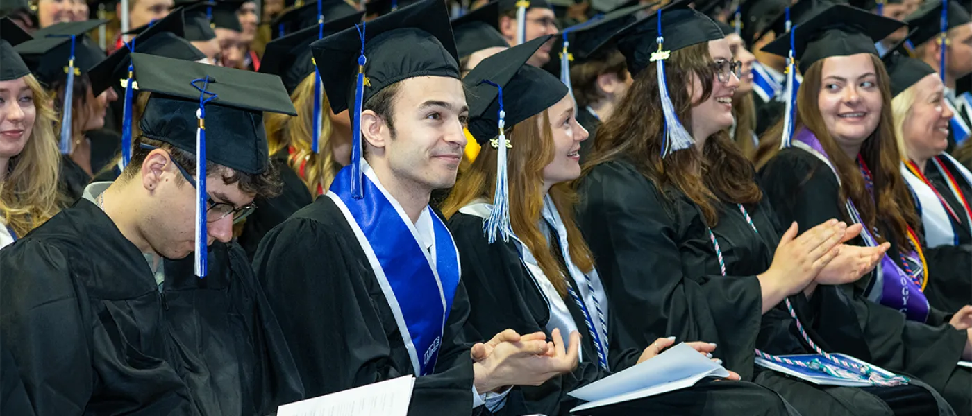 A line of sitting graduating students clap during the commencement ceremony