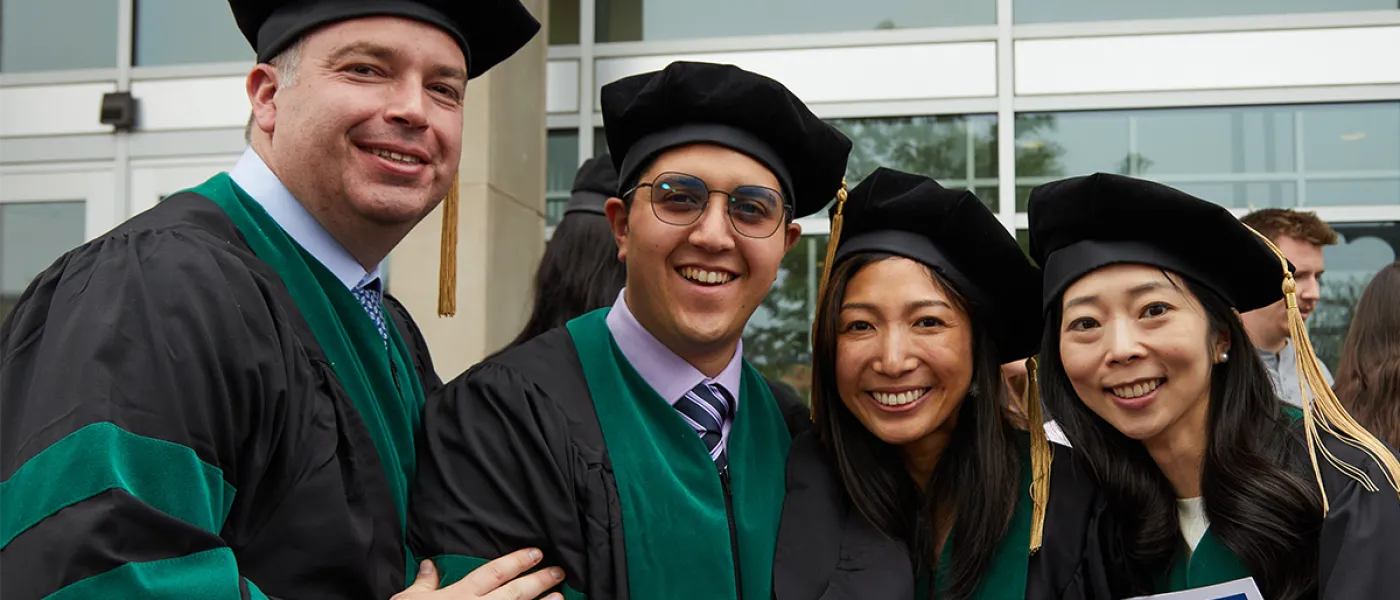 Four C O M students pose in their green and black graduation regalia