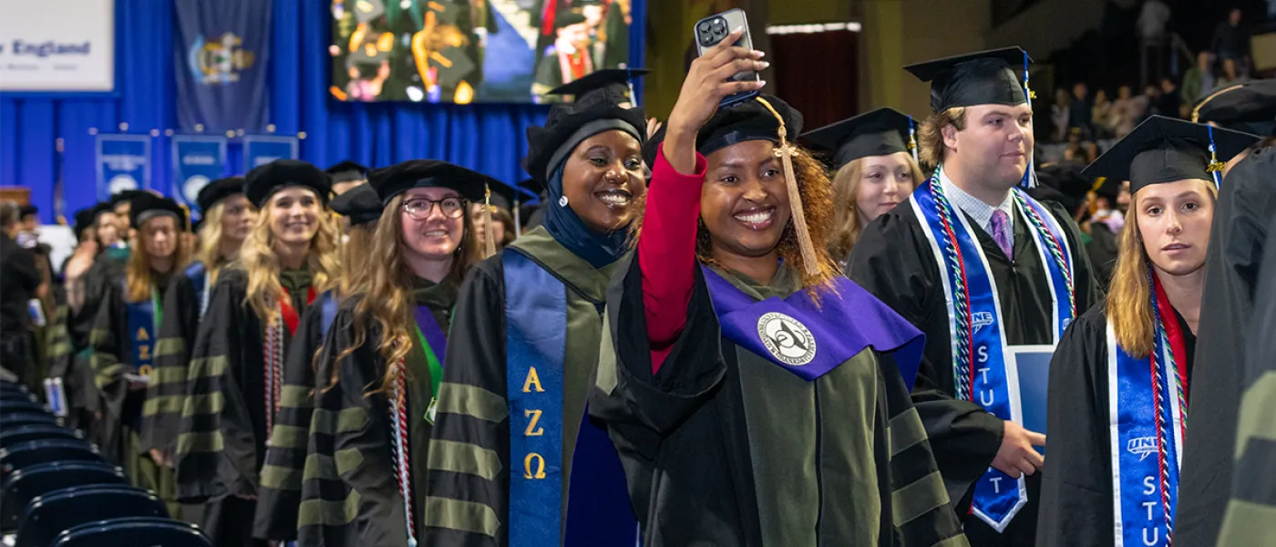 A student records commencement on their cell phone from the crowd