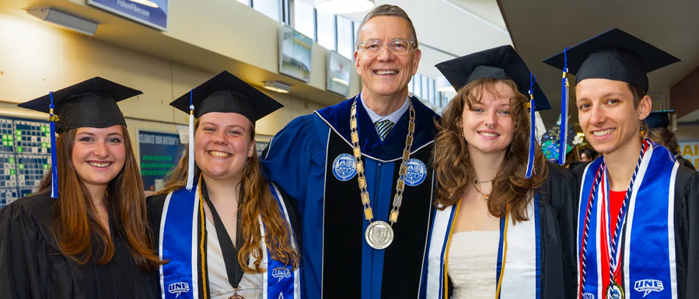 Four students in U N E regalia pose with President Herbert in the middle