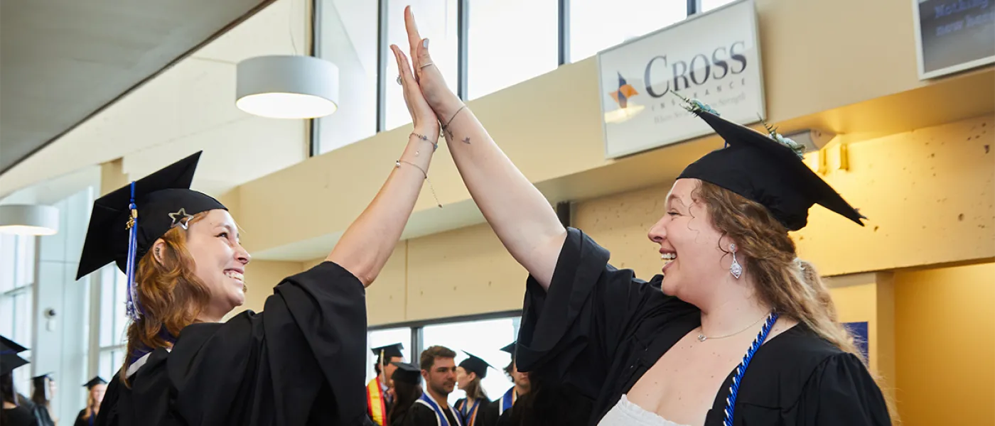 Two students high five in their cap and gowns