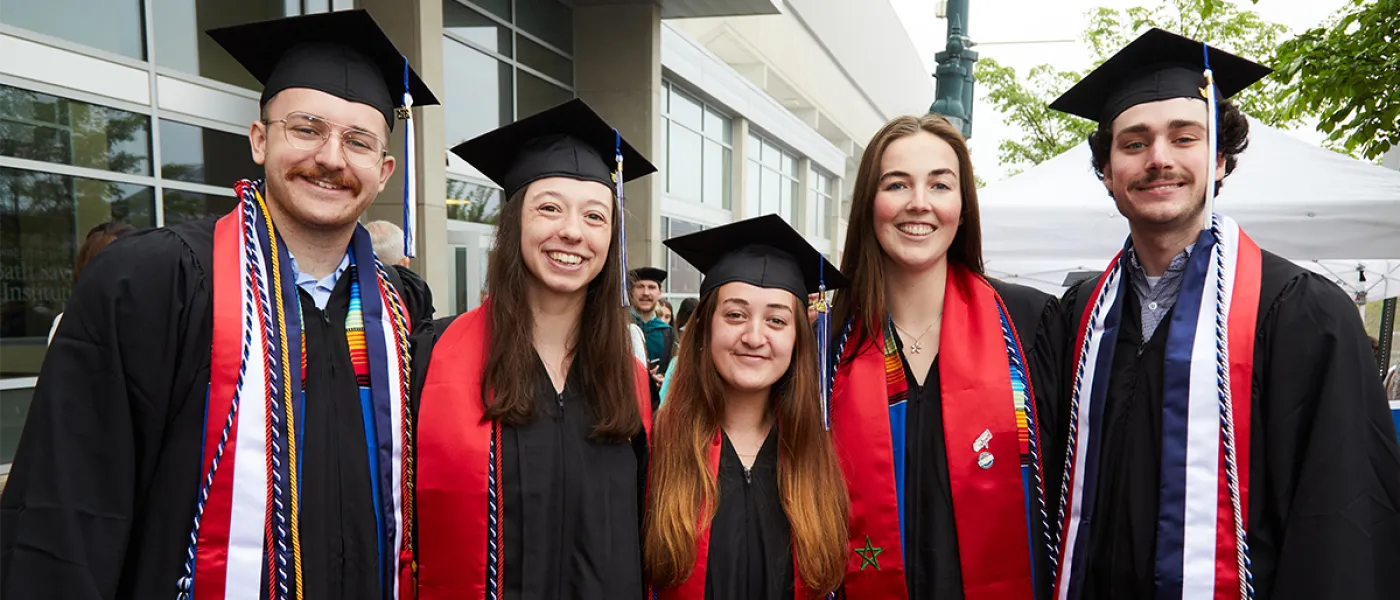 A group of five undergraduate students pose in their regalia with red stoles