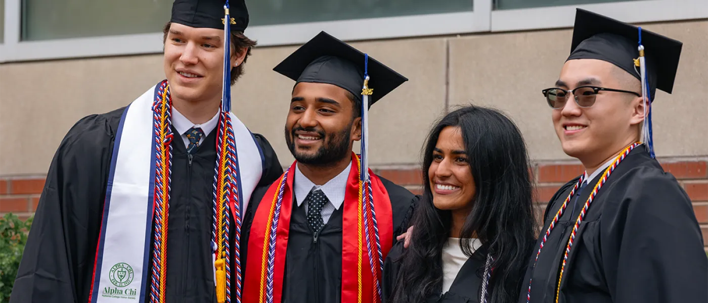 Four graduating students smile and pose in their regalia