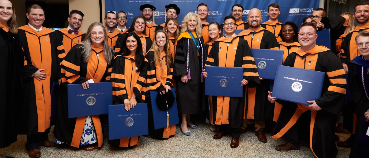 A large group of W C H P graduating students pose with their degrees in their black and orange regalia