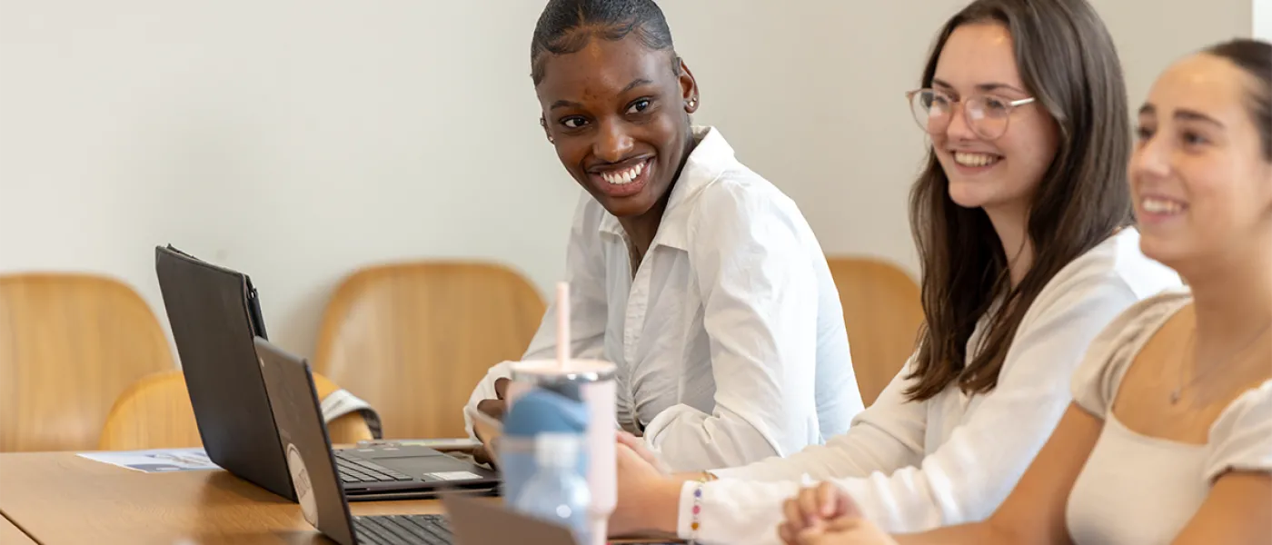 Three students smile at each other as they sit in front of their open laptops