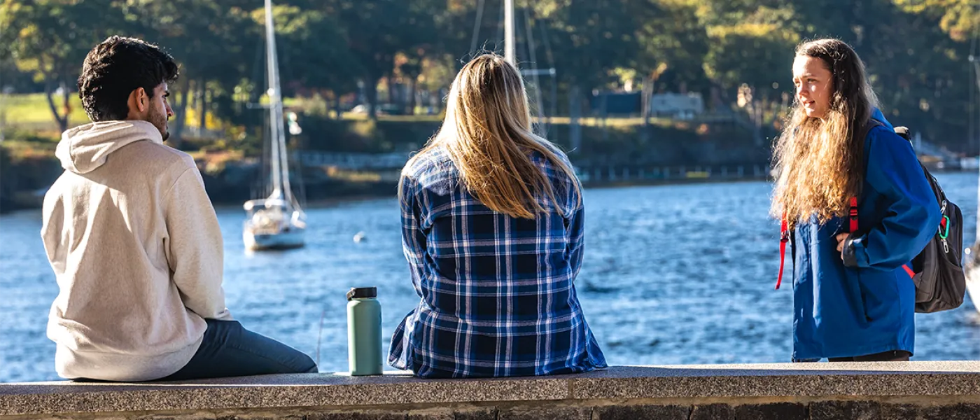 Three students talk in front of the Saco River