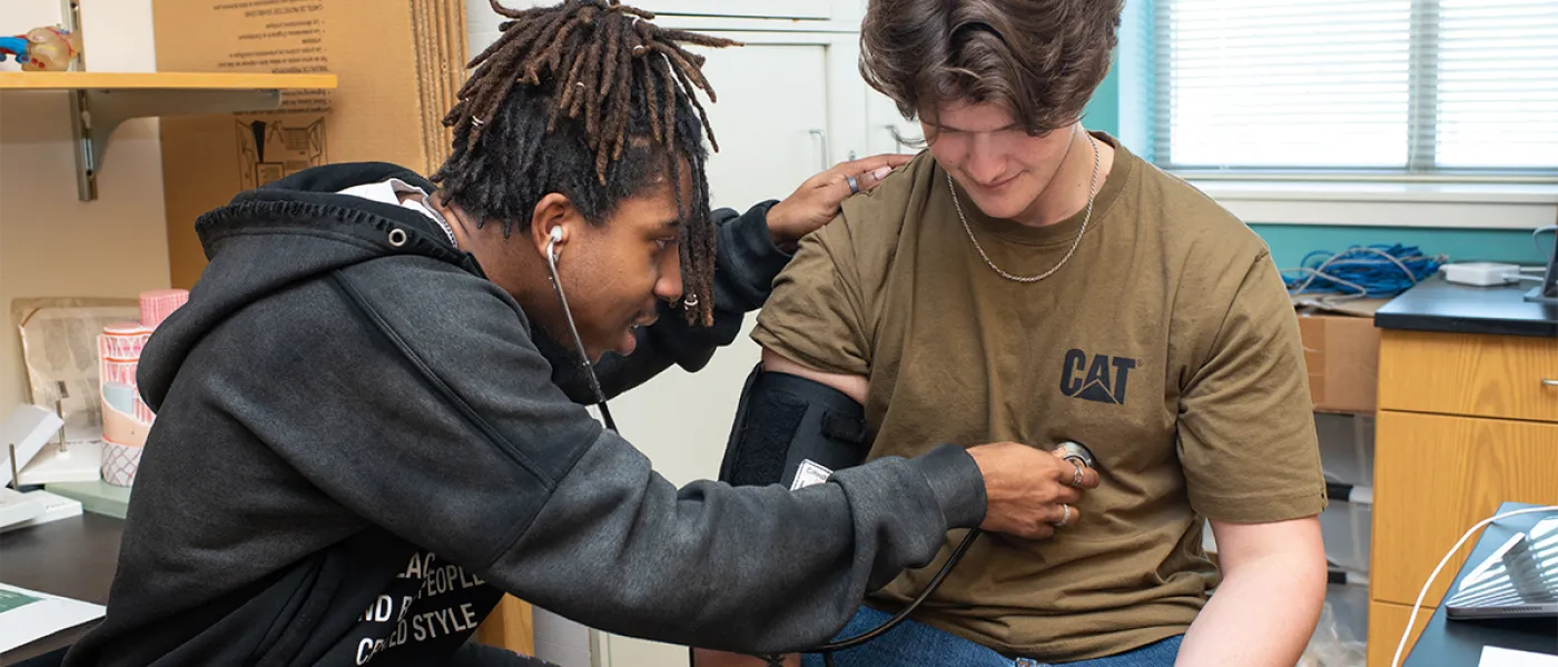 A student listens to another student's heartbeat using a stethoscope in a lab
