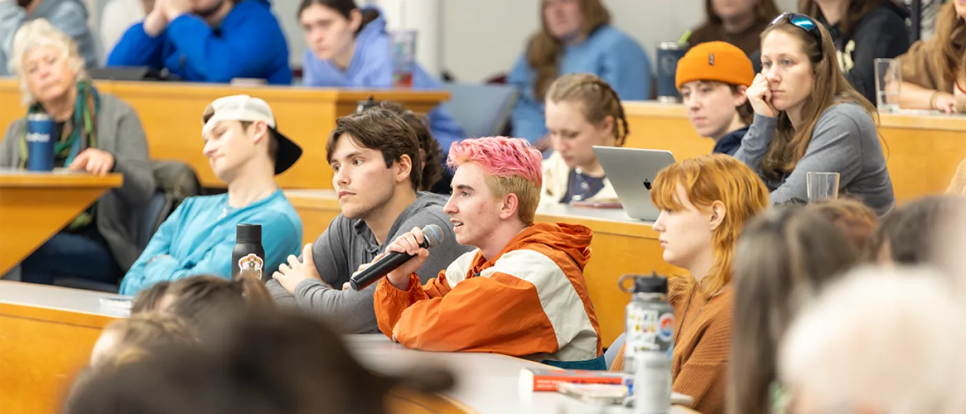 A student speaks into a microphone from the audience in a lecture hall
