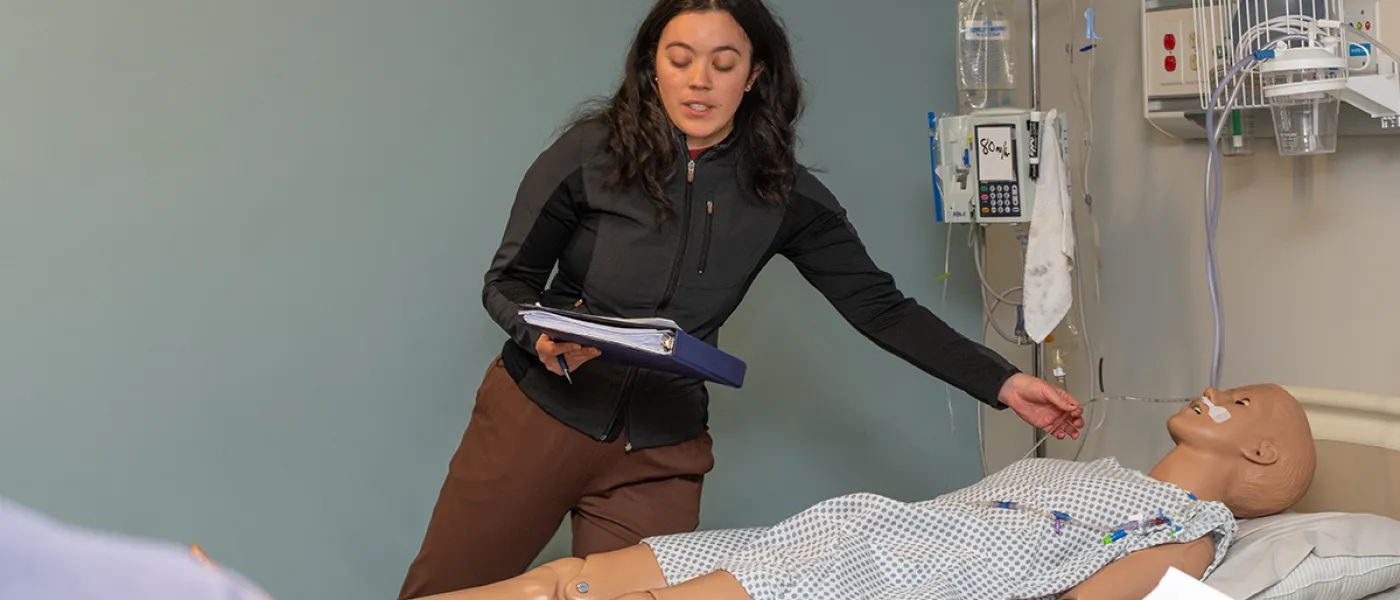 A student reads from their binder while working on a patient simulator in the Sim Lab