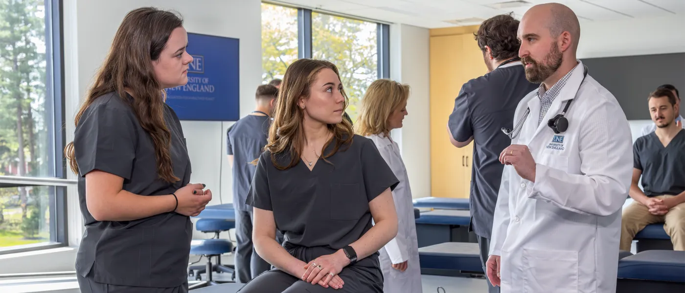 A professor speaks to two physician assistant students in a skills lab