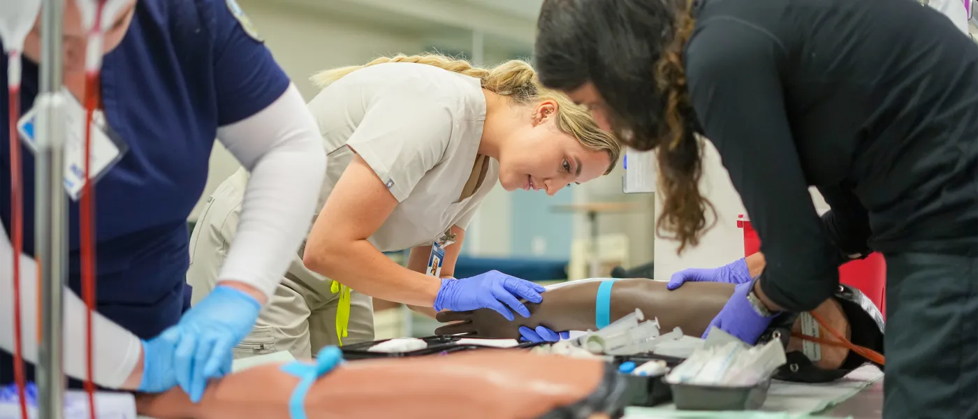 Two nursing students prepare a patient simulator arm for an I V line