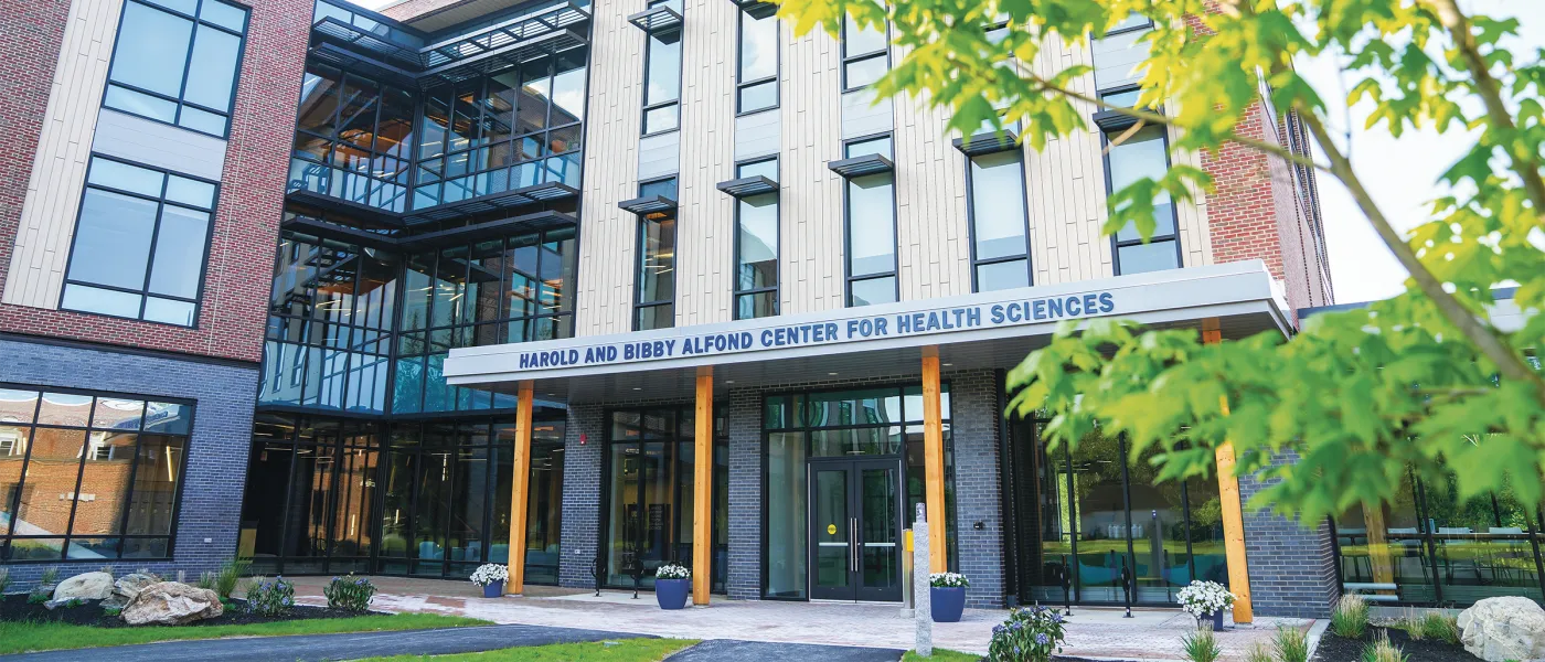 Entrance to Harold and Bibby Alfond Center for Health Sciences building with glass doors, brick facade, and landscaping.