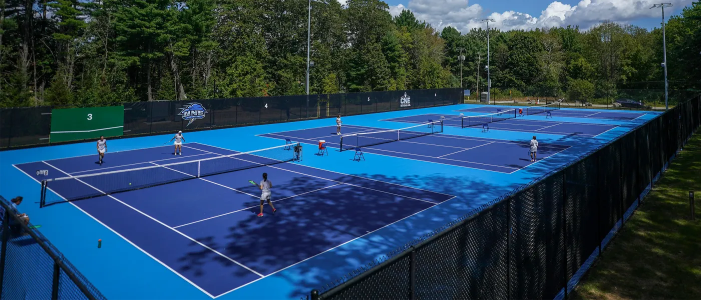 Wide view of the Blue Cyclone Complex showing all six tennis courts with players competing during UNE's inaugural tennis season.