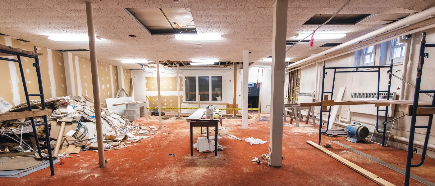 Demolished interior space with damaged ceiling tiles, construction debris, red carpeting, and exposed walls during renovation.