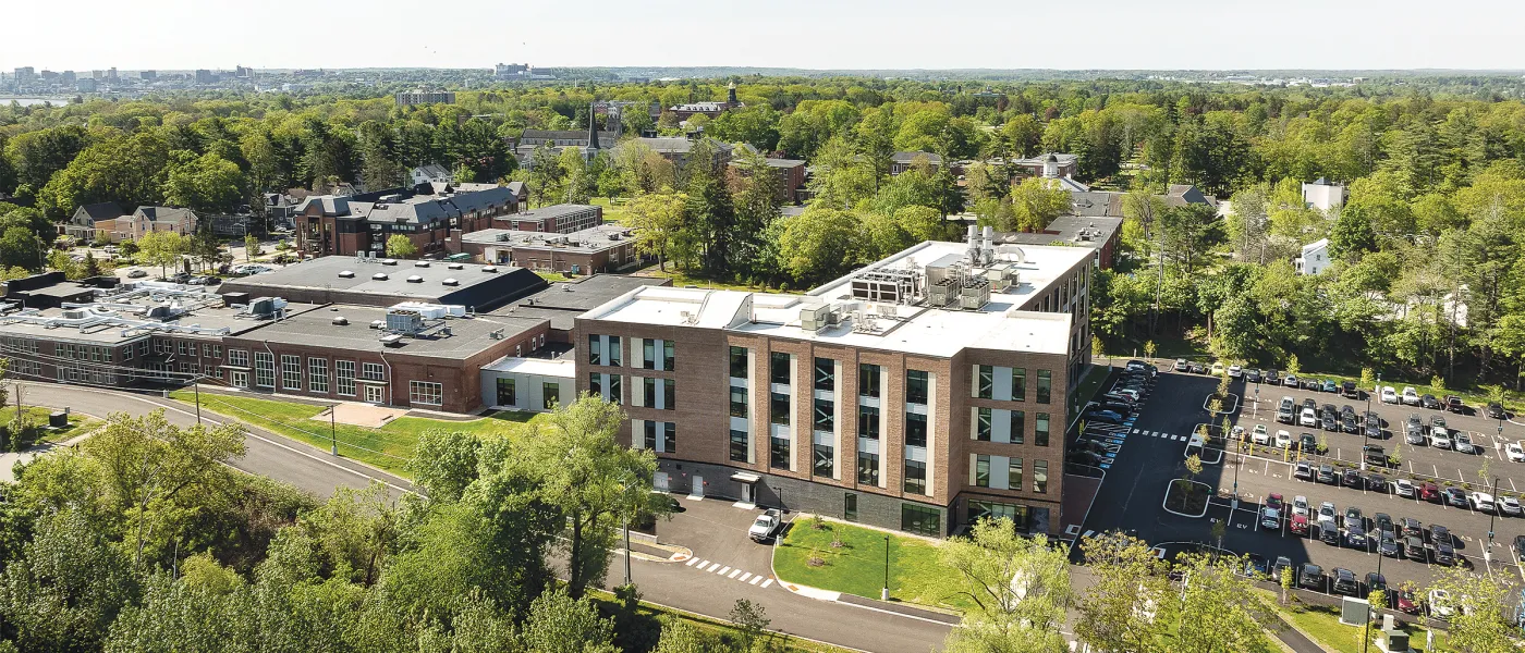 Aerial view of modern brick UNE health sciences campus building surrounded by trees and parking lots.