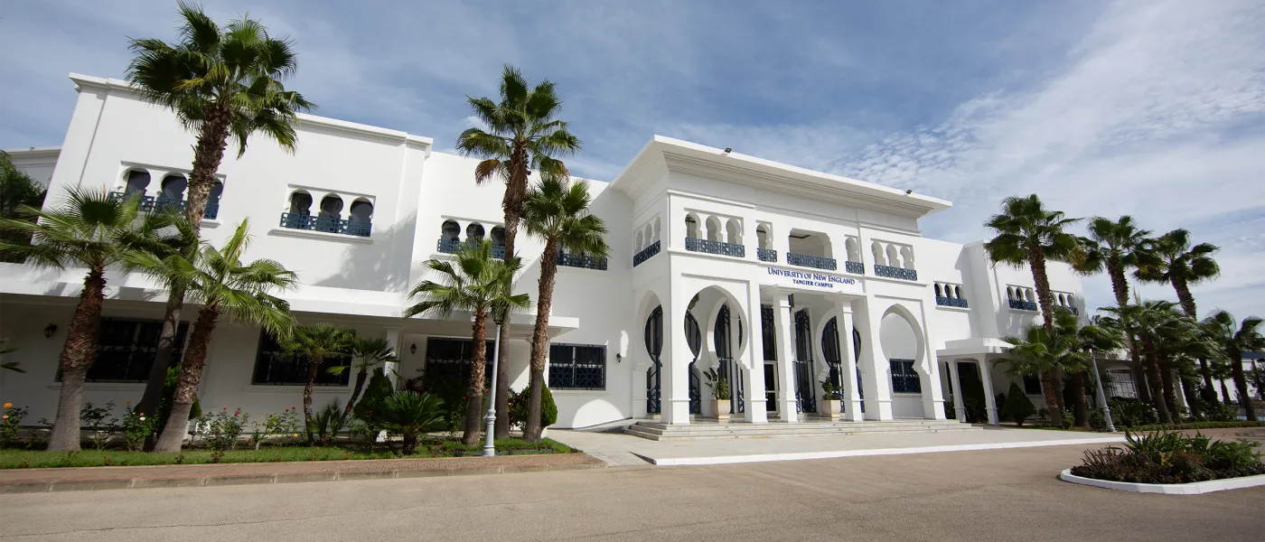 Wide view of white Moroccan-style campus buildings featuring traditional arched entryways, decorative balconies, and palm trees along a manicured lawn.