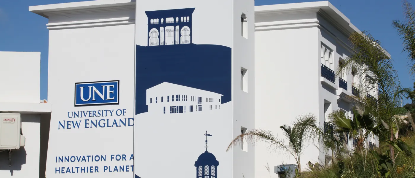 Exterior wall at UNE Tangier Campus featuring university branding and architectural illustration showing building with distinctive arched windows.