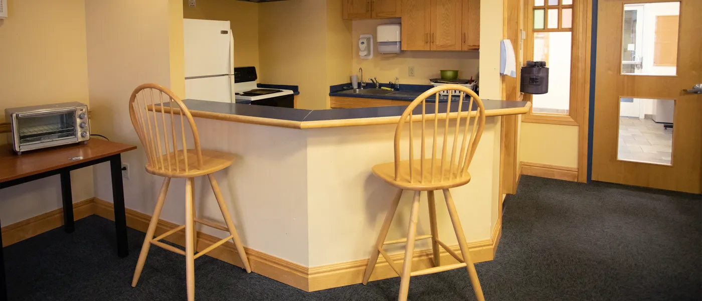 Shared apartment kitchen with breakfast bar, two wooden stools, white appliances, oak cabinets, and a toaster oven on a side table.
