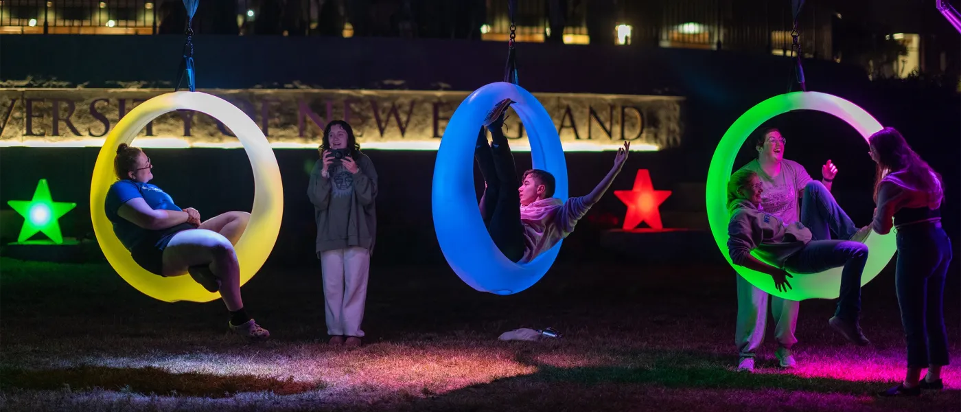 U N E students play on illuminated ring swings at night during a Week of Welcome event.