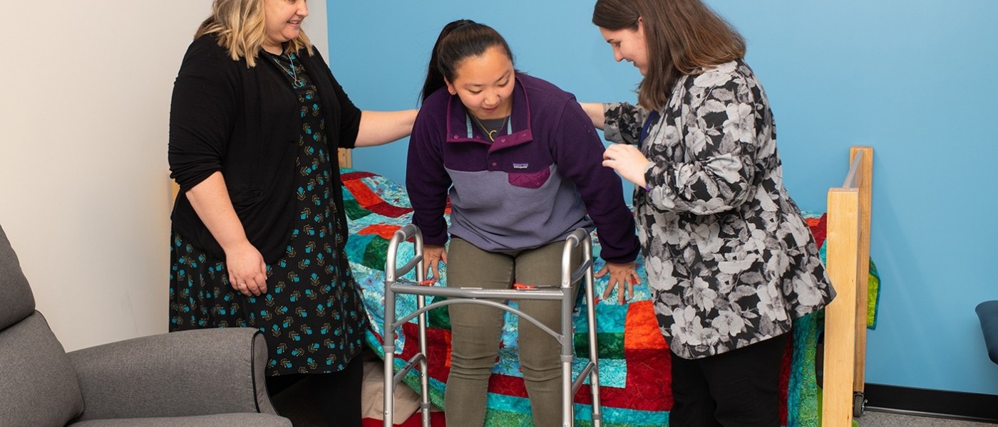Two students help a patient use a walker