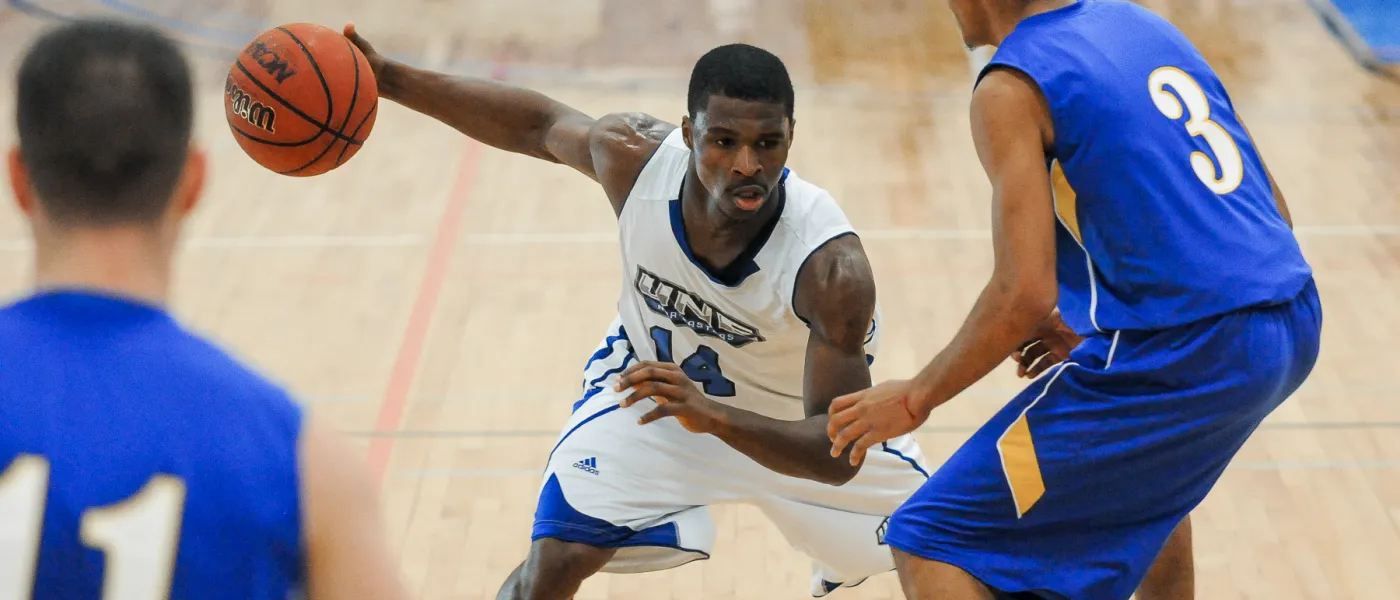 U N E basketball player Charles Fenner dribbles between opponents