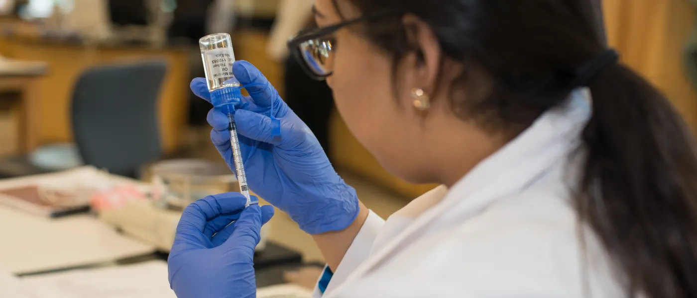 U N E College of Pharmacy student pipettes at a vet session