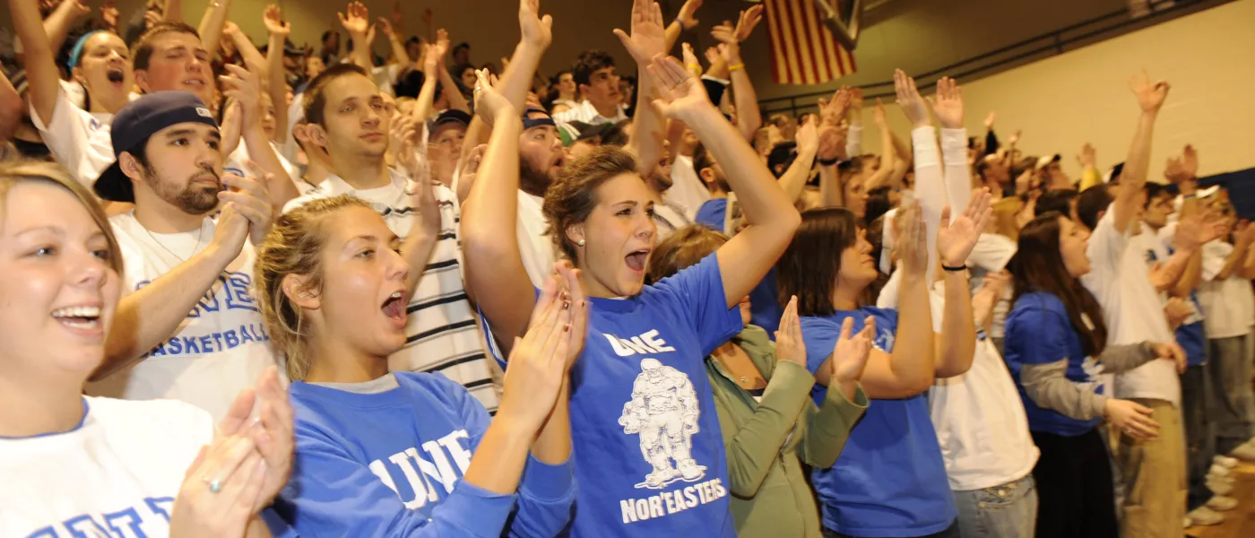 A group of students stand and cheer at a U N E basketball game
