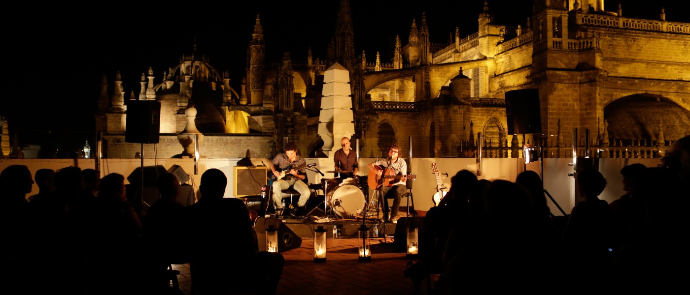 People listen to an evening musical performance at an outdoor plaza in Seville
