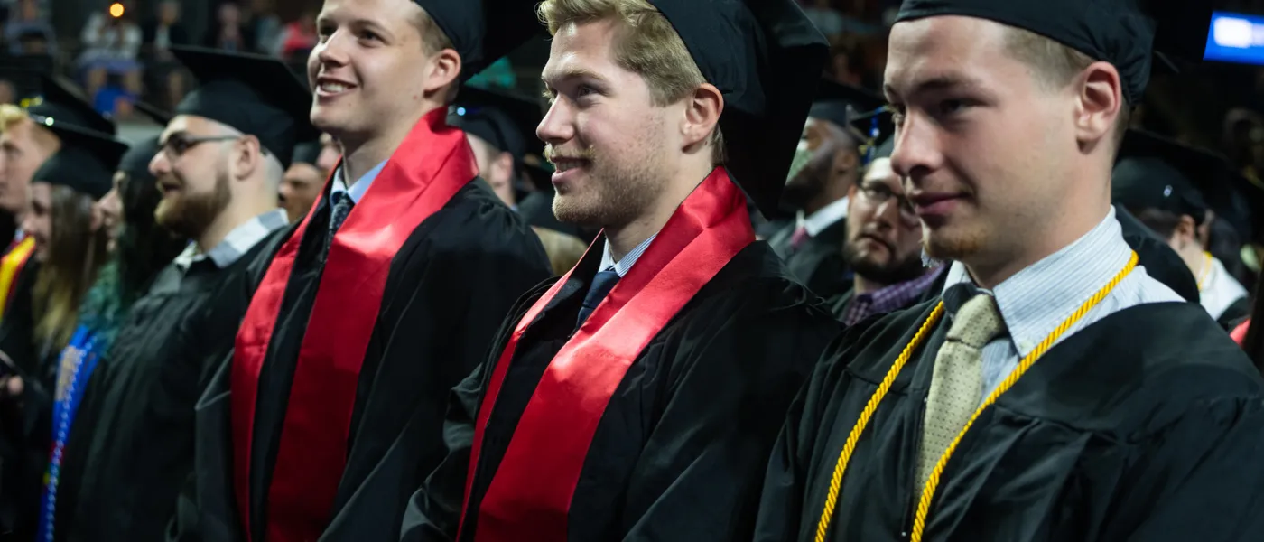 Three male students stand at graduation