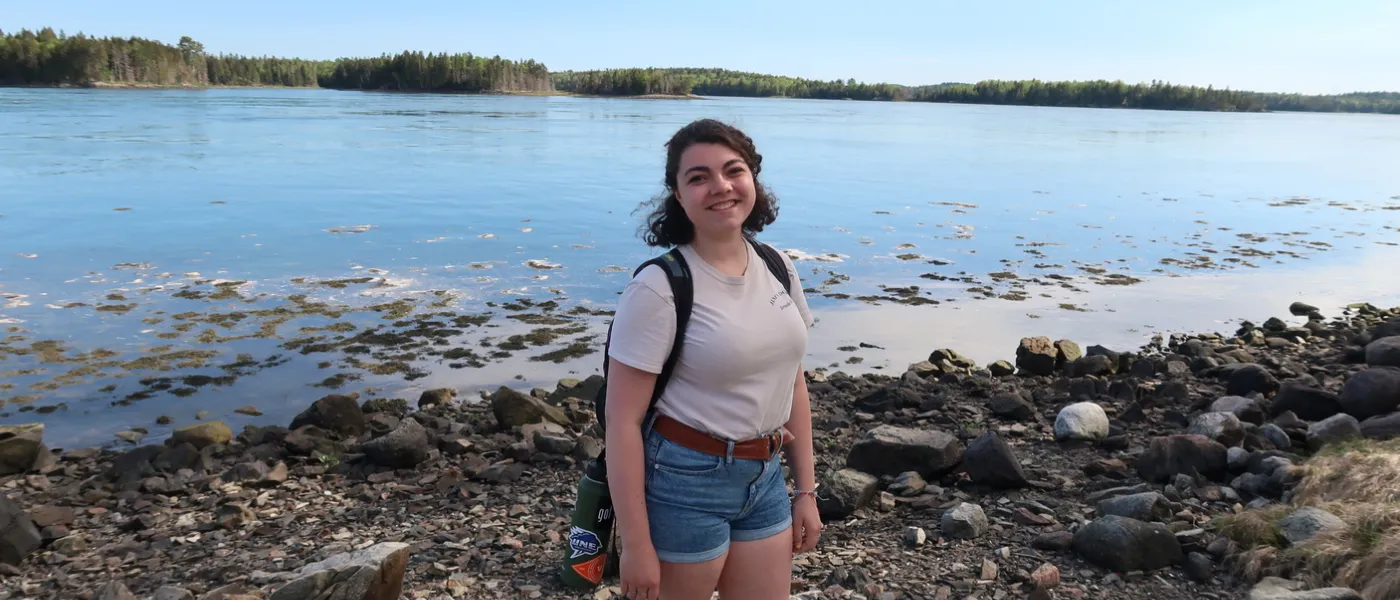 A female student poses on a rocky beach with the ocean behind her