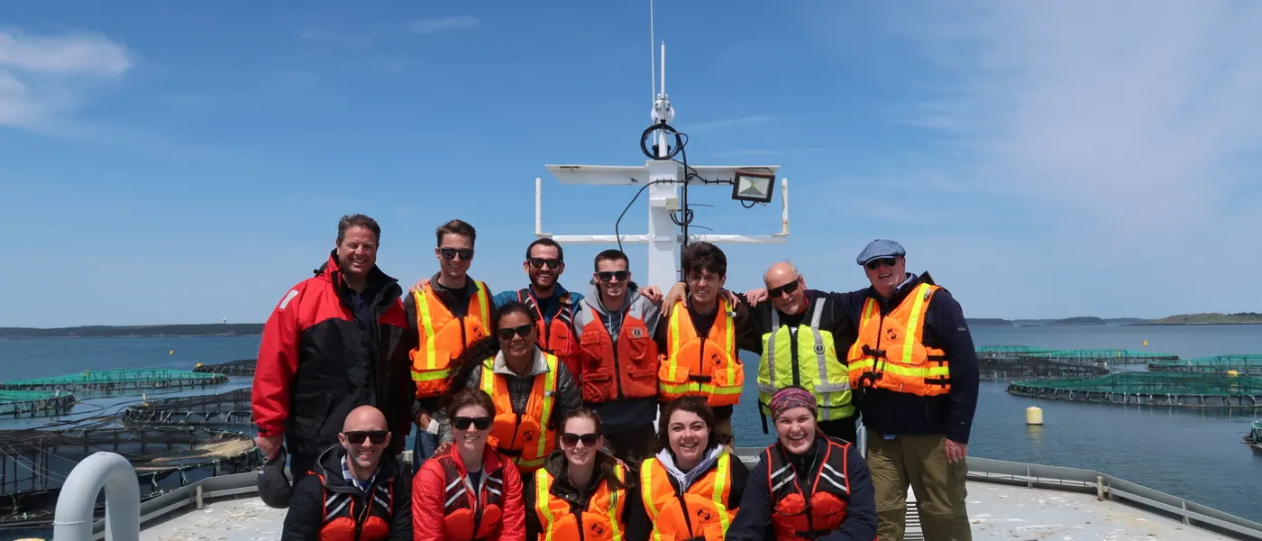 A group of students wearing orange lifejackets pose on a boat