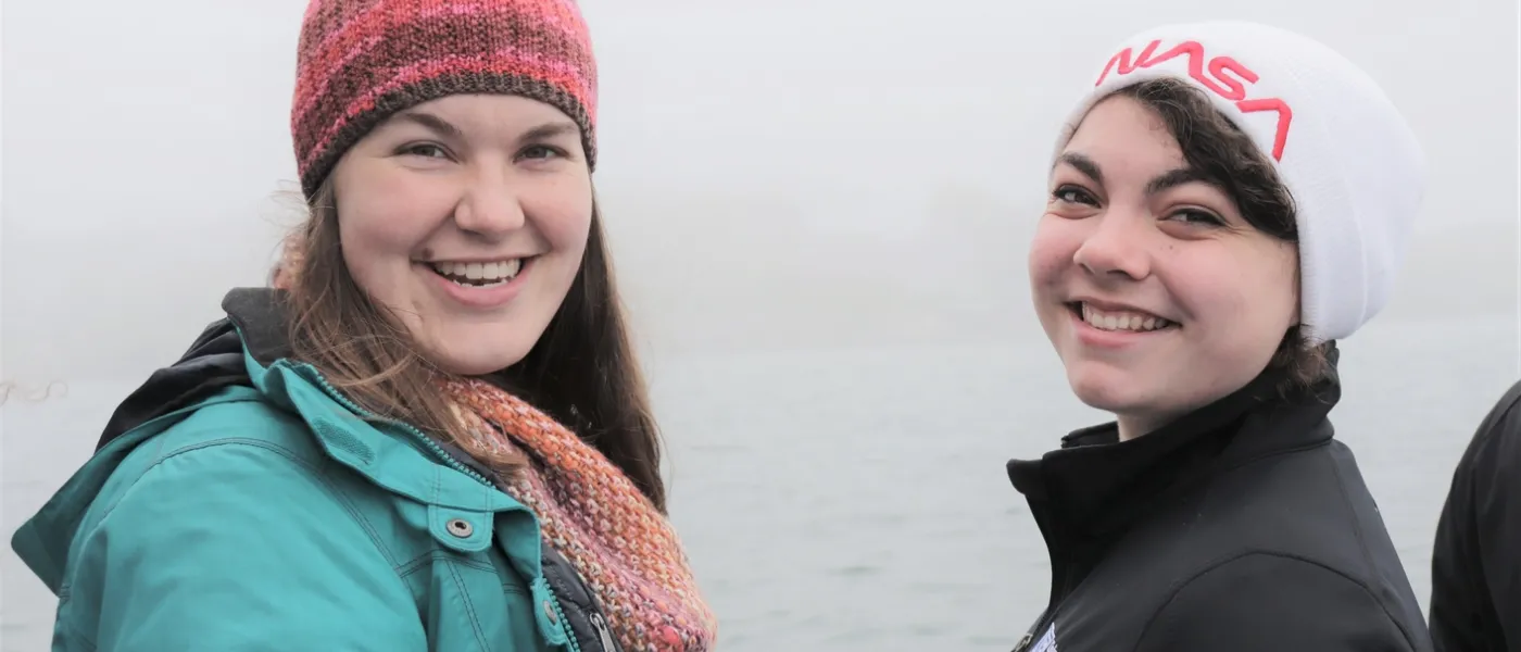 Two female students pose in the cold with water in the background
