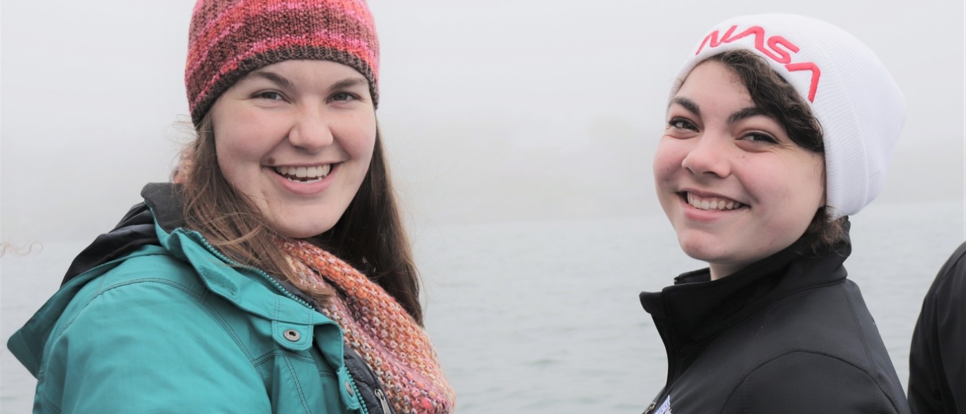 Two female students pose in the cold with water in the background