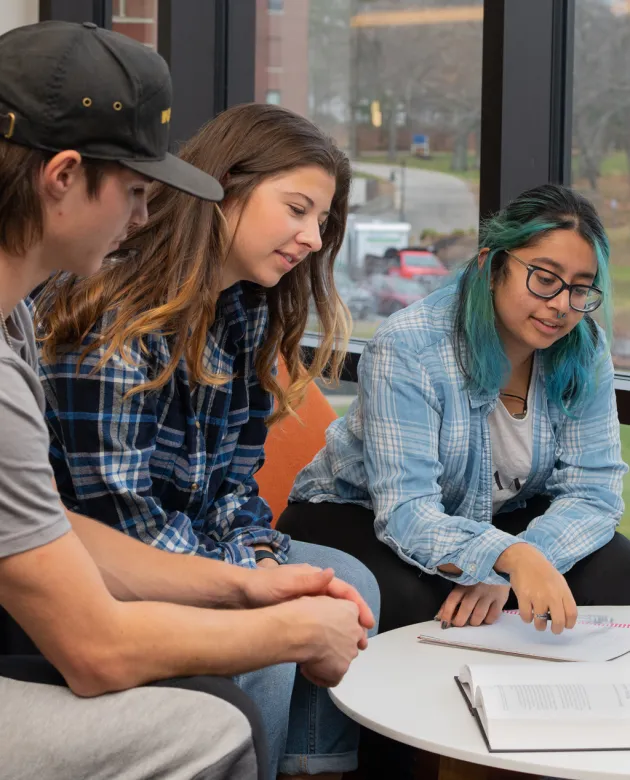 Three students sit at a table and read class notes off a notebook