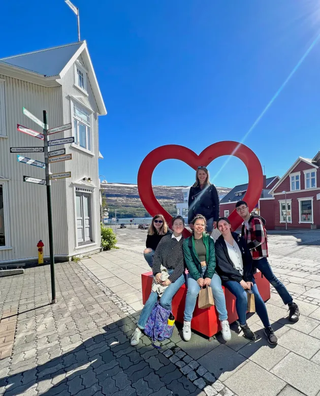 A group of students sit under a heart-shaped sculpture in the middle of a Akureyri street