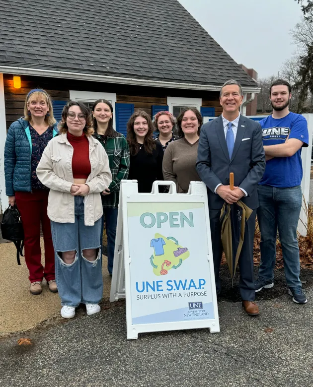 President Herbert stands with U N E students behind an "Open" sign for the Swap Shop
