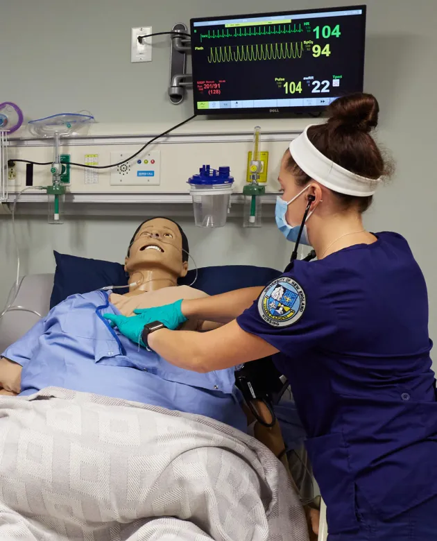 A nursing student assists a patient simulator in the simulation lab