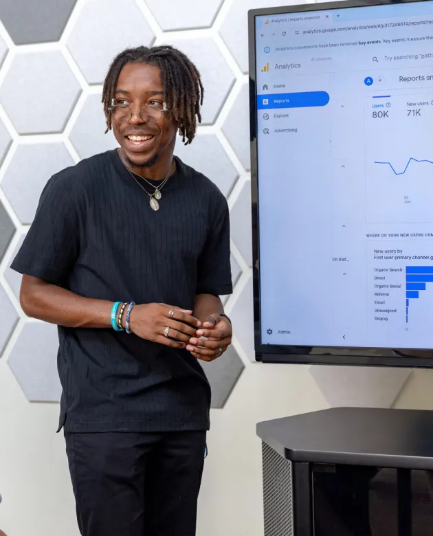 A student stands next to a large monitor showing site analytics