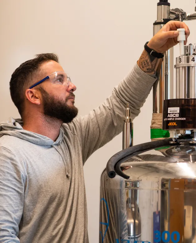 A student in blue rubber gloves prepares samples above a tank in a chemistry lab