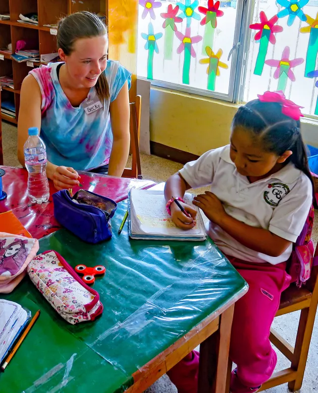 A student in a study abroad program in Mexico sits with an elementary school student in a classroom