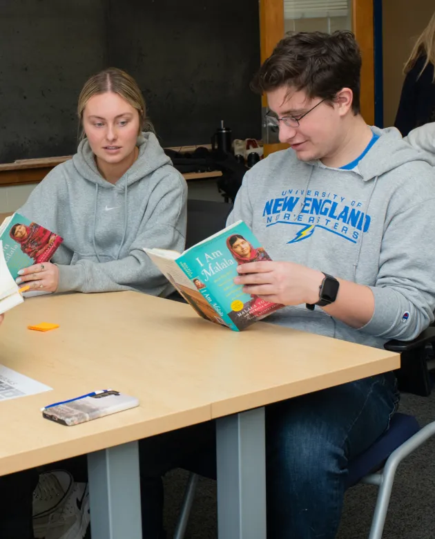 Two students read from "I Am Malala" in a U N E class