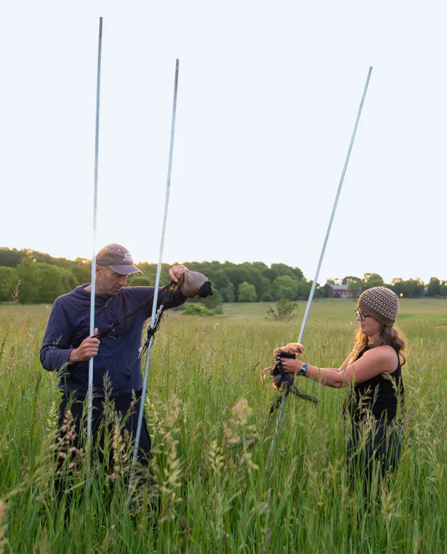 A professor and student hold up ends of a net while standing in a grassy field