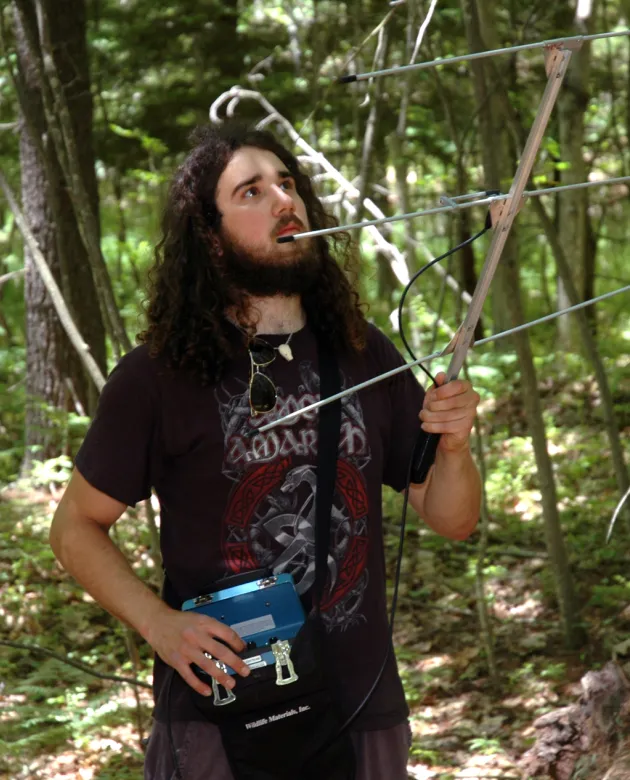 An environmental studies student uses a radio telemetry while walking through a forest