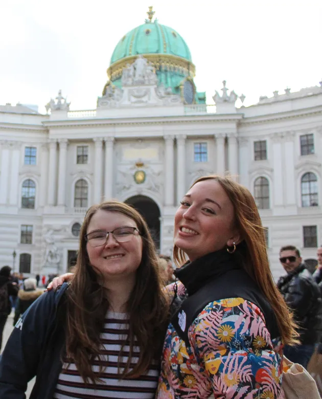 Two students stand in front of a white building with a green and gold dome