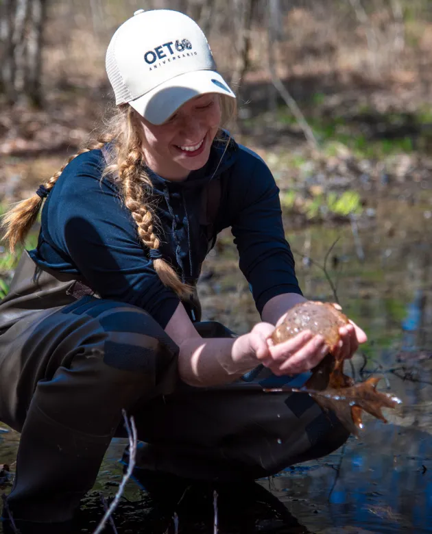 A student holds a frog egg mass while standing in a vernal pool