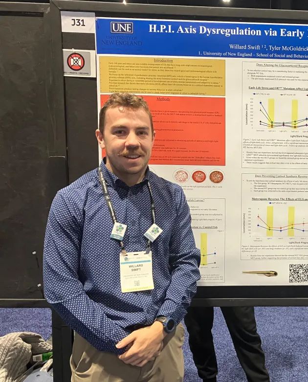 A UNE student stands in front of his research poster