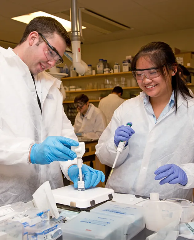 Two students fill pipettes in a lab